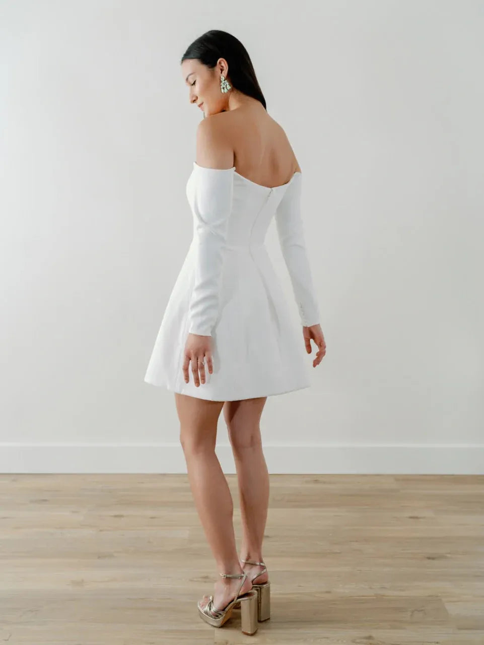 Woman wearing a white off-shoulder dress with long sleeves on a plain background