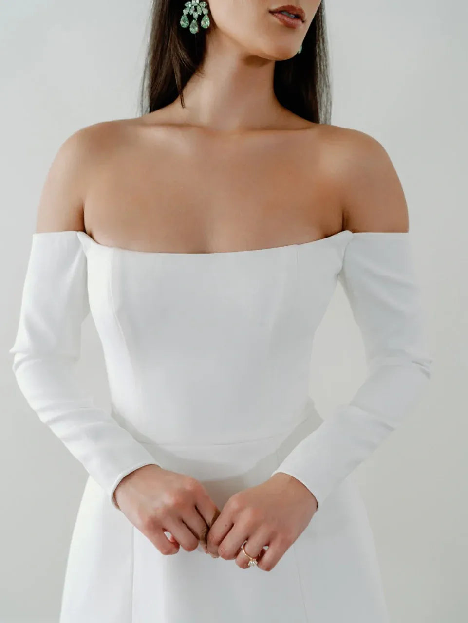 White off-shoulder long-sleeve dress worn by a model against a plain background