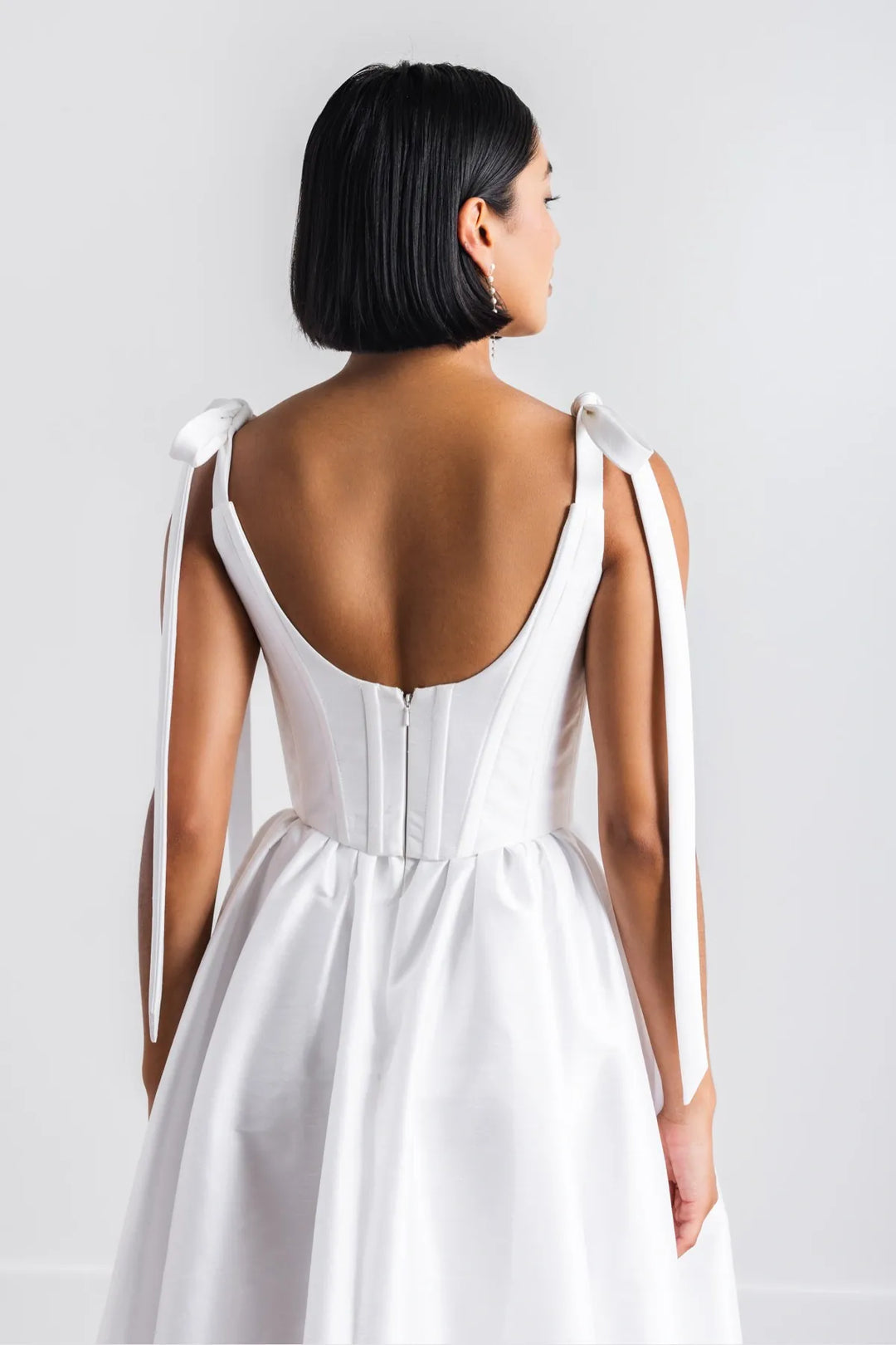 Woman wearing a white dress with thin straps on a plain background