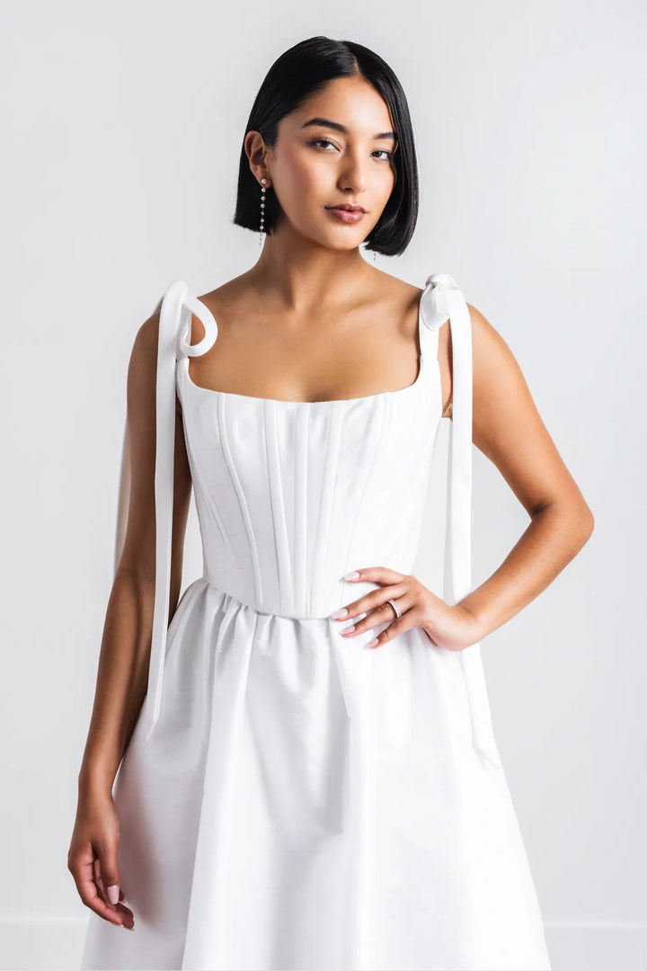 Woman wearing a white dress with thin straps against a plain background