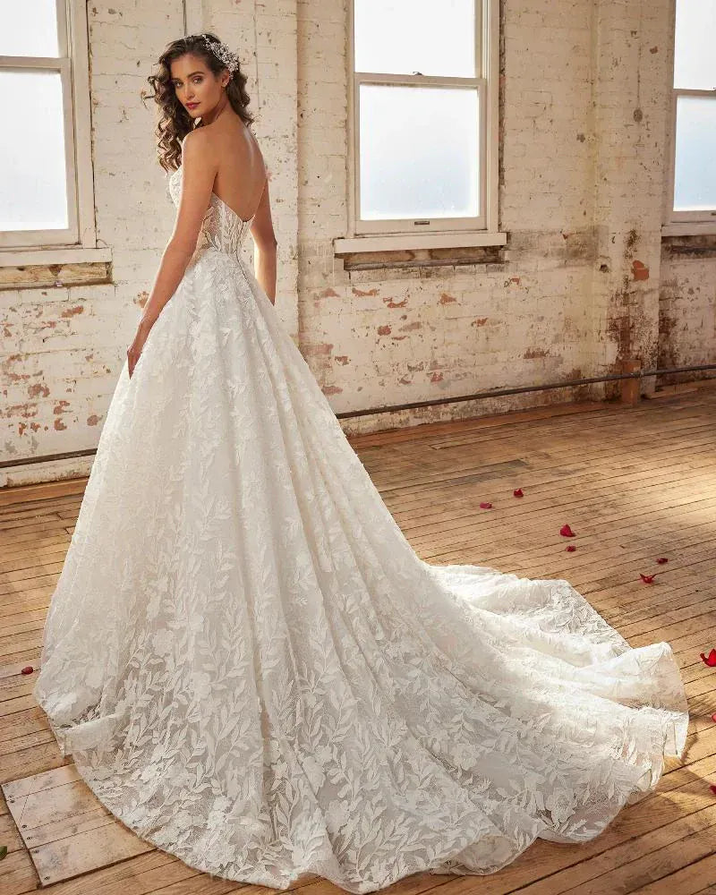 Woman in a white lace wedding dress standing in a room with brick walls and wooden floors.