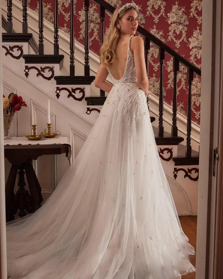 Woman in a white wedding dress standing in a room with decorative wallpaper and staircase.