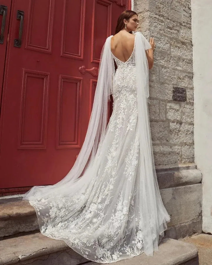 Woman in a white lace wedding dress standing against a red door.