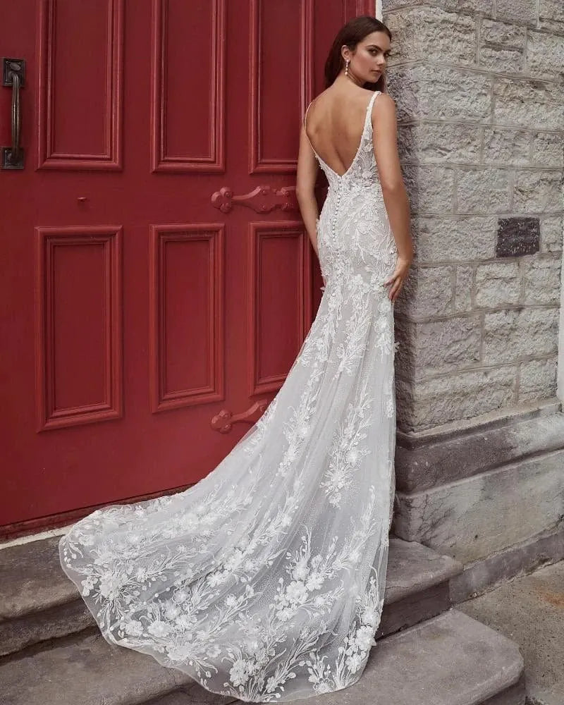 Woman in a white lace wedding dress standing against a red door and stone wall.