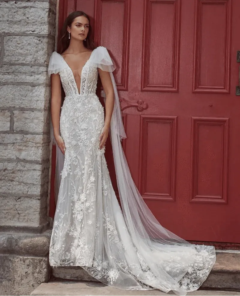 Woman in a white lace wedding dress standing in front of a red door.