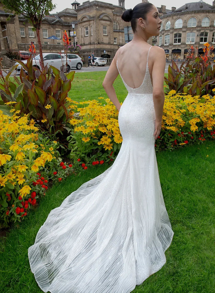 Woman in a white dress standing in a garden with flowers and a building in the background