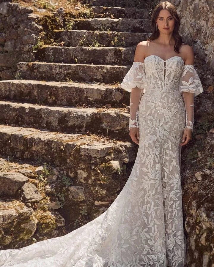 Woman in a white lace dress standing on stone steps.