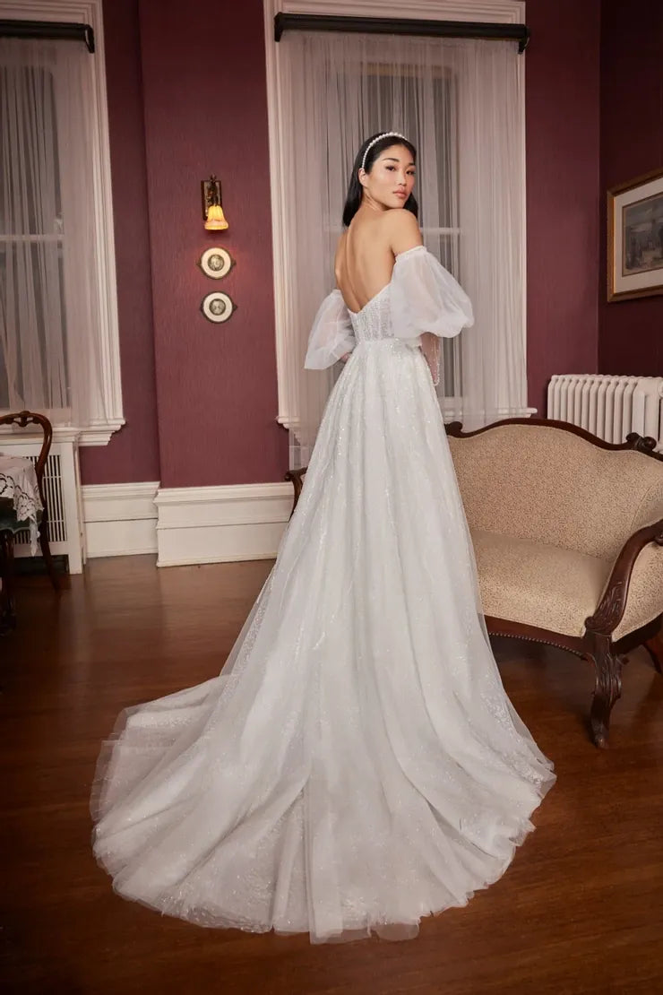 Woman in a white wedding dress standing in a room with a purple wall and wooden floor.