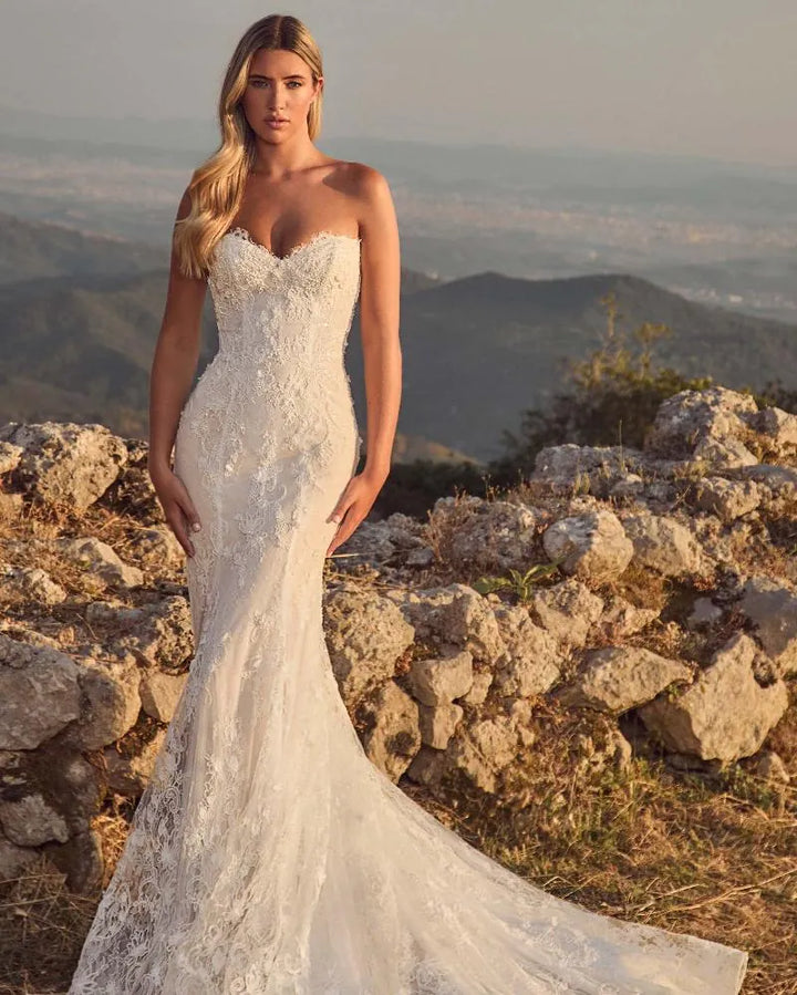 Woman in a white wedding dress standing on a rocky mountain top with a scenic view.
