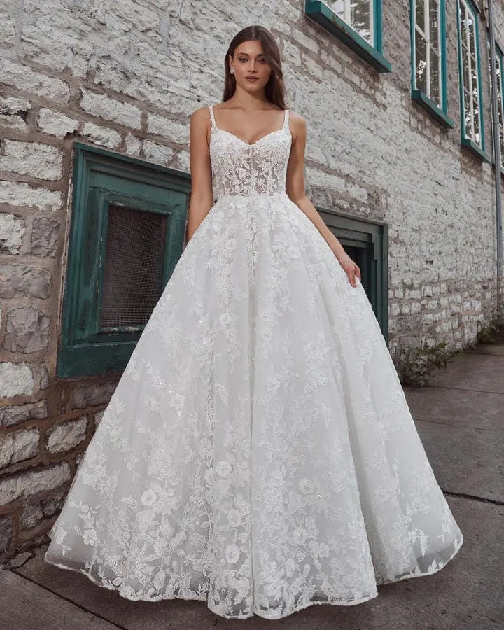 Woman wearing a white lace wedding dress standing in front of a brick wall.