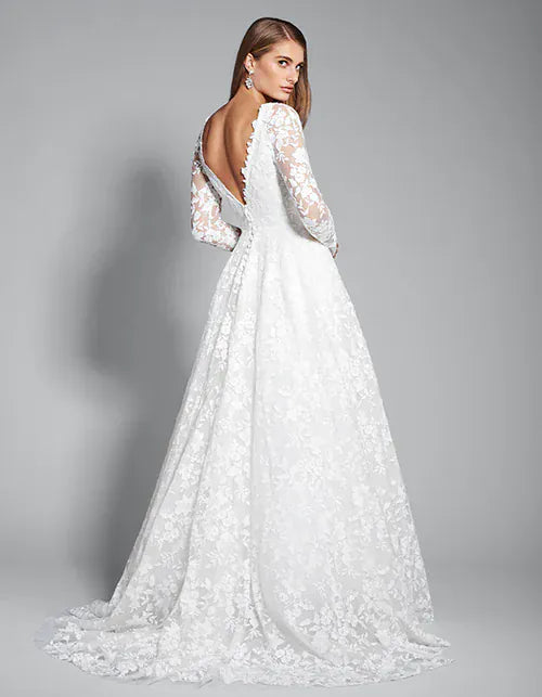 A white lace wedding gown with long sheer sleeves and a dramatic open back, shown on a model from behind against a neutral gray studio background.