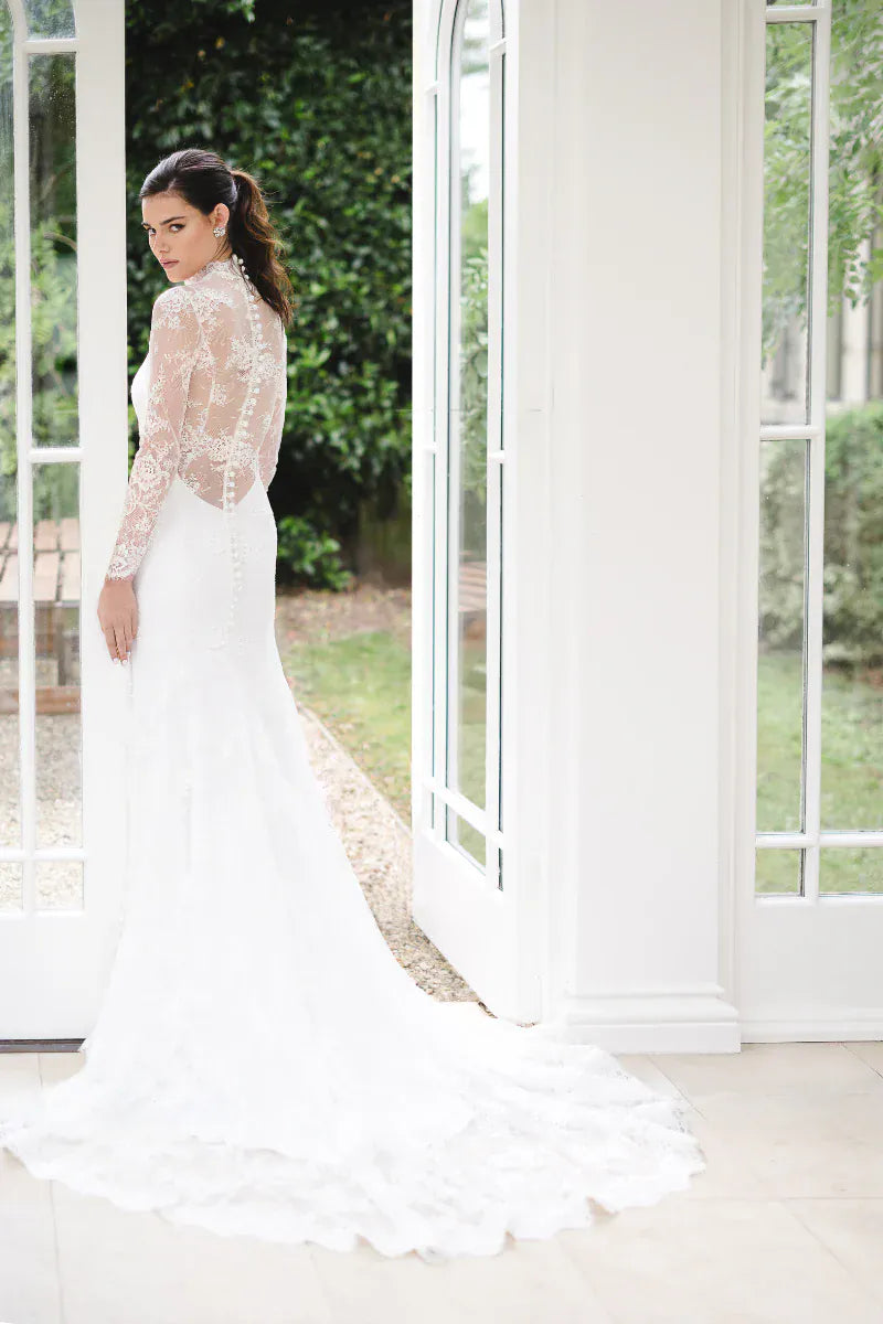 Woman in a white wedding dress standing in a room with large windows.