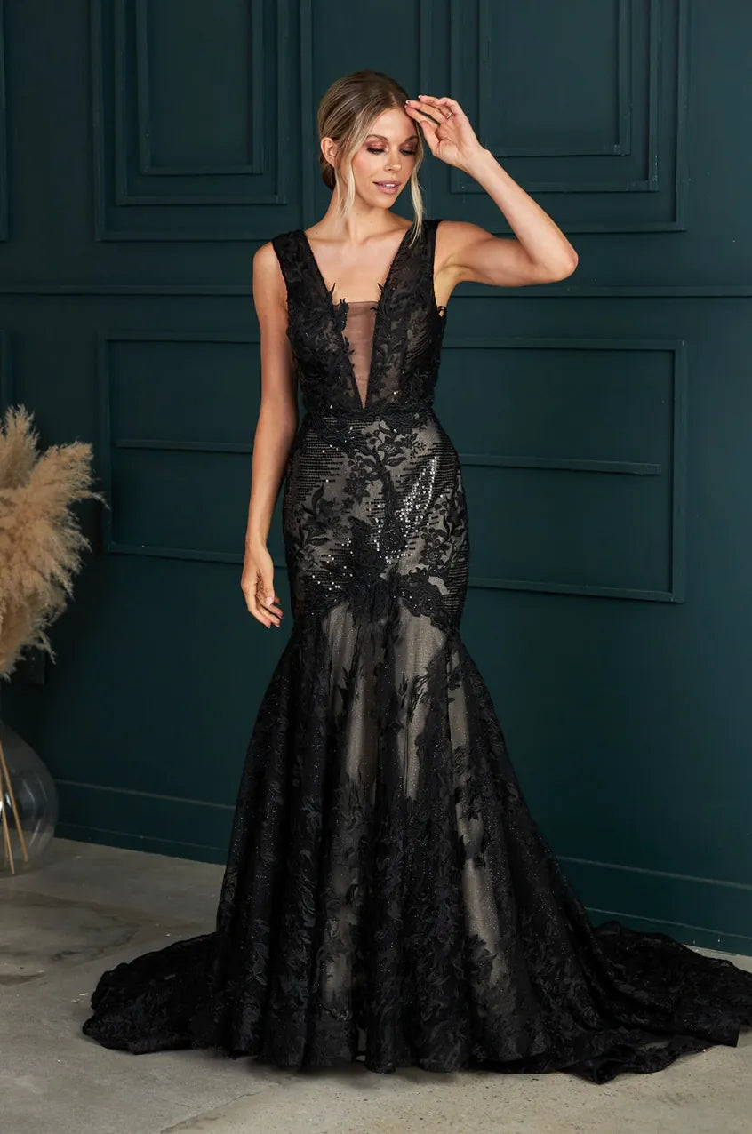Woman wearing a black lace evening gown against a dark blue wall.