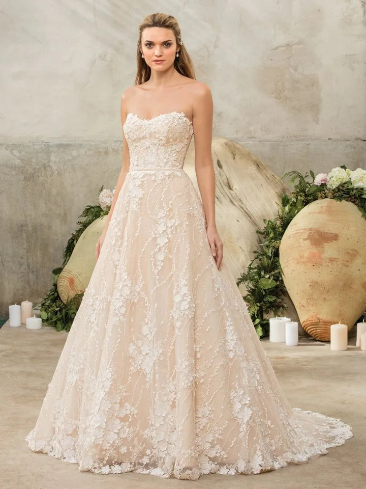 Model wearing a strapless lace wedding dress in a decorated setting with flowers and candles.