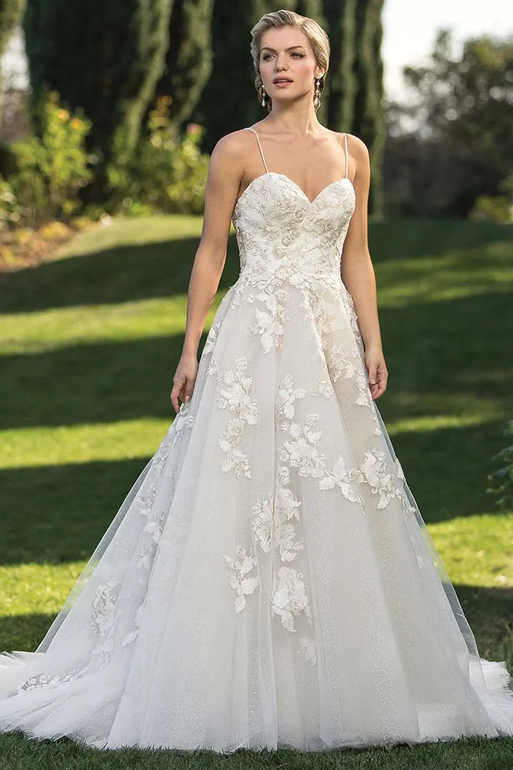 Woman wearing a white wedding dress with floral details standing outdoors on grass.