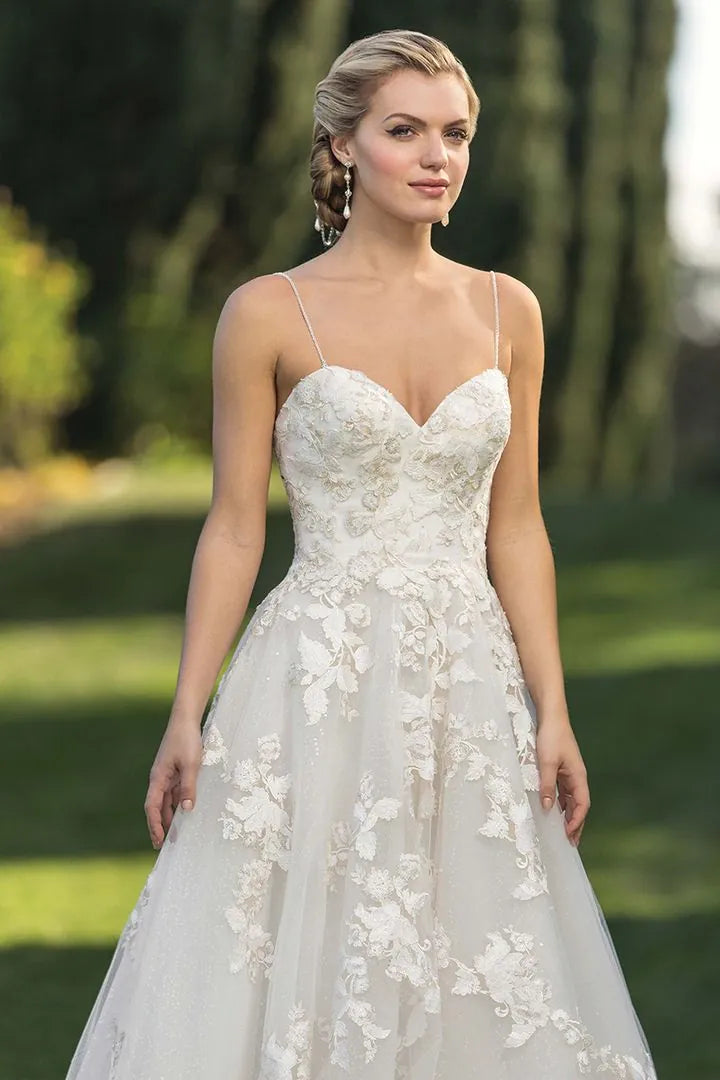 Woman wearing a white lace wedding dress outdoors with greenery in the background