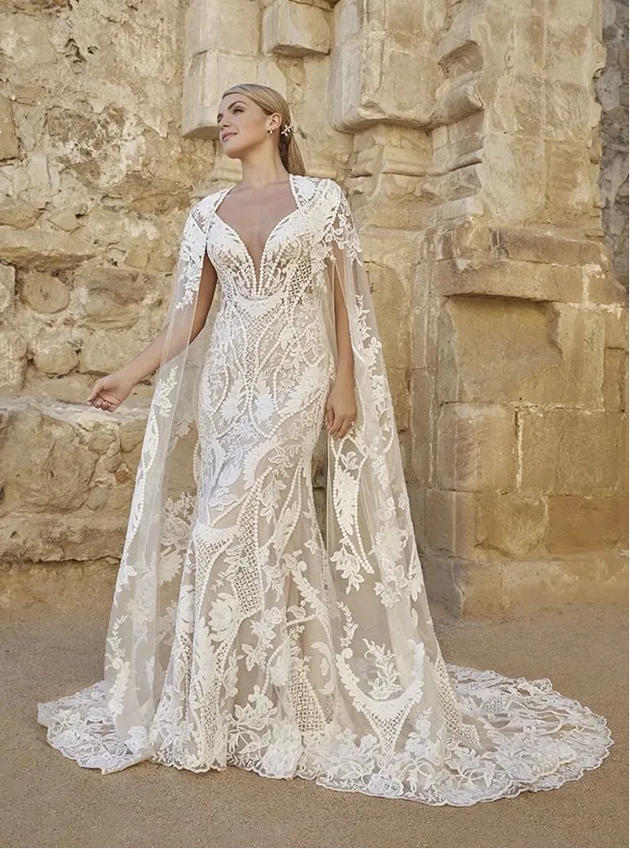 Woman in a white lace wedding dress standing in front of stone ruins.