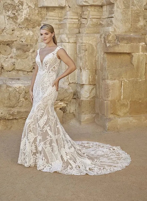 Woman in a lace wedding dress standing against a stone wall.