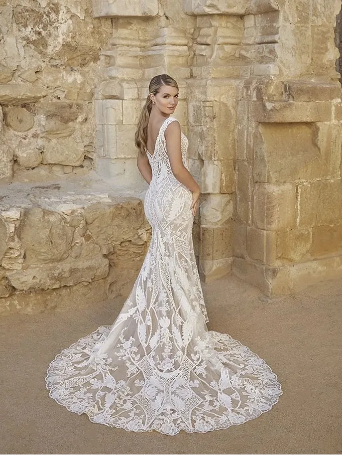 Woman in a white lace wedding dress standing against a stone wall.