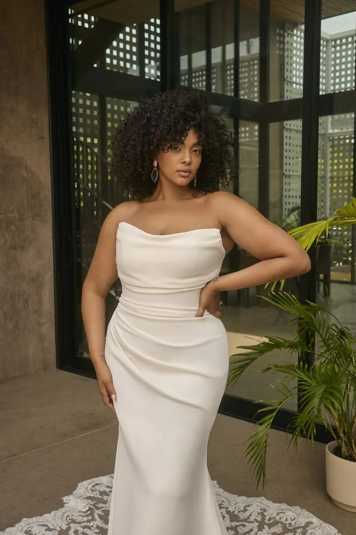 Woman in a white strapless dress standing indoors with plants in the background