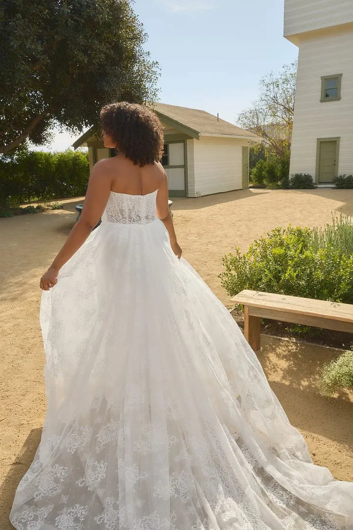 Woman in a white wedding dress standing outdoors with a building and trees in the background