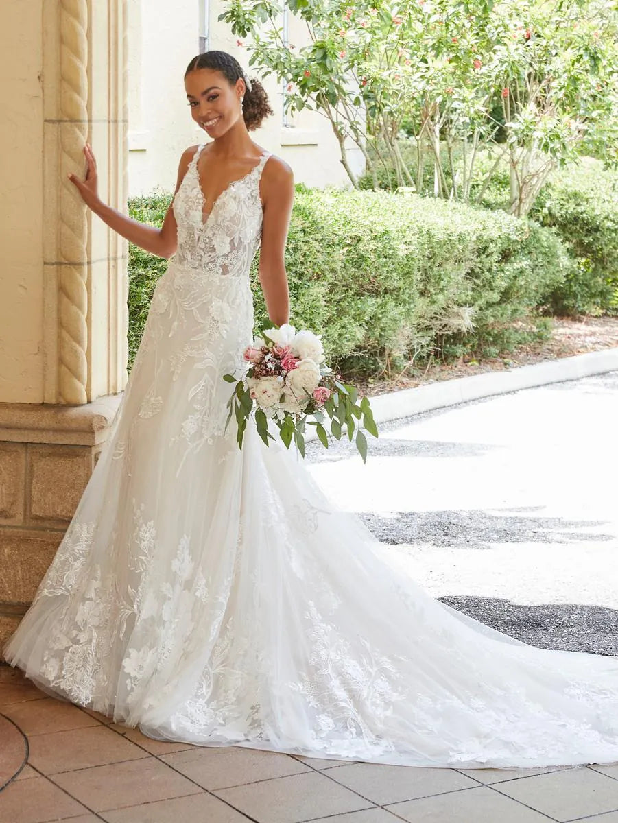 Woman in a white lace wedding dress holding flowers outdoors.