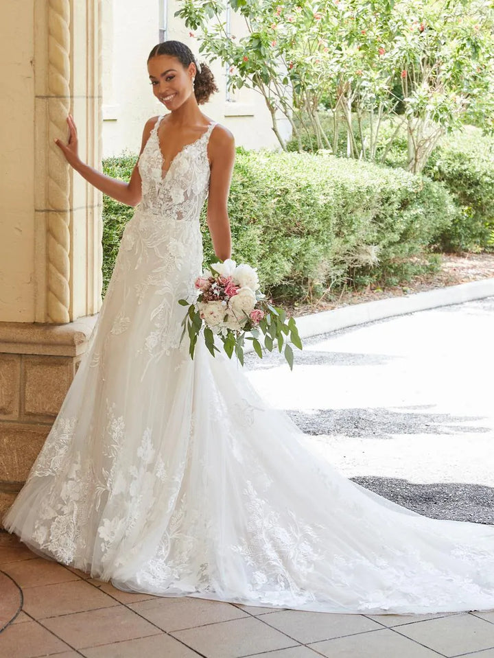 Woman in a white lace wedding dress holding flowers outdoors.