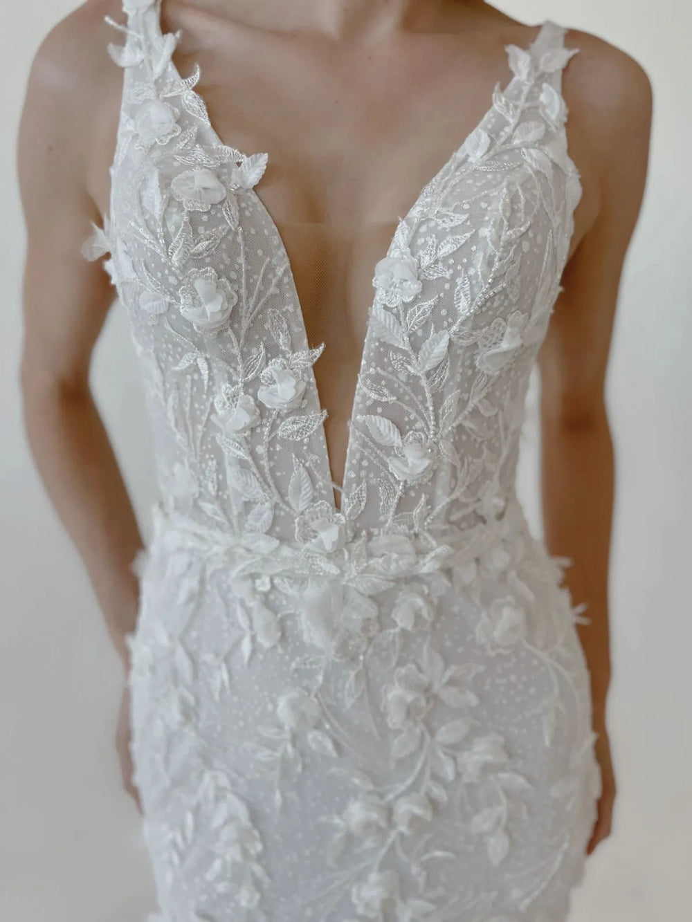 White lace wedding dress with a deep neckline on a white background