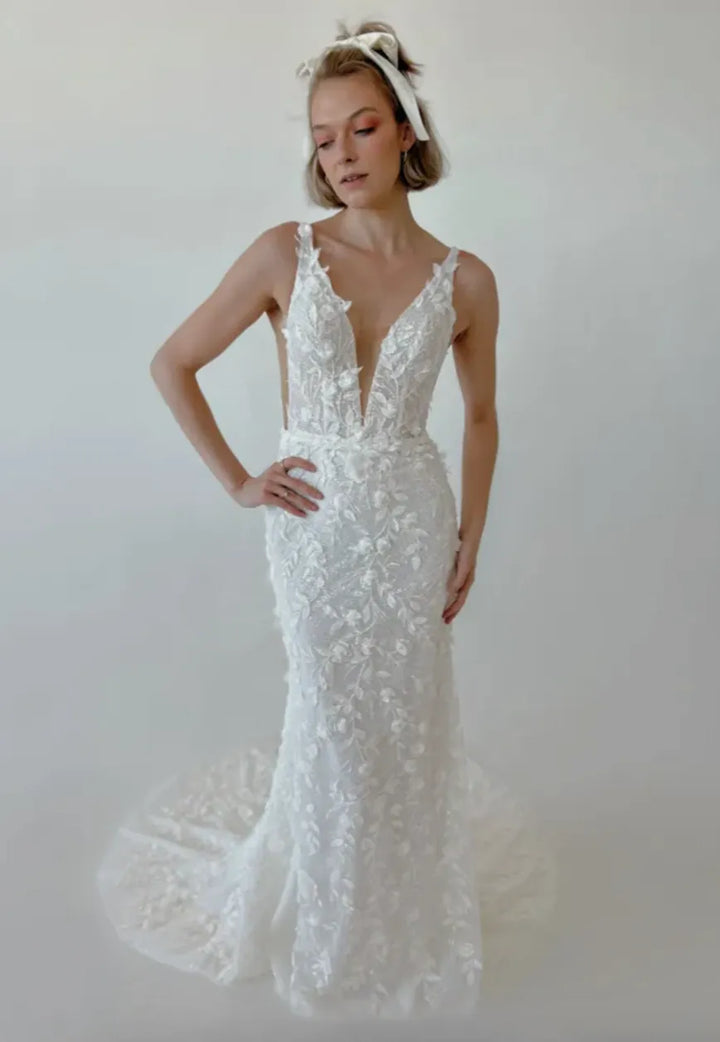 Woman wearing a white lace wedding dress against a plain background