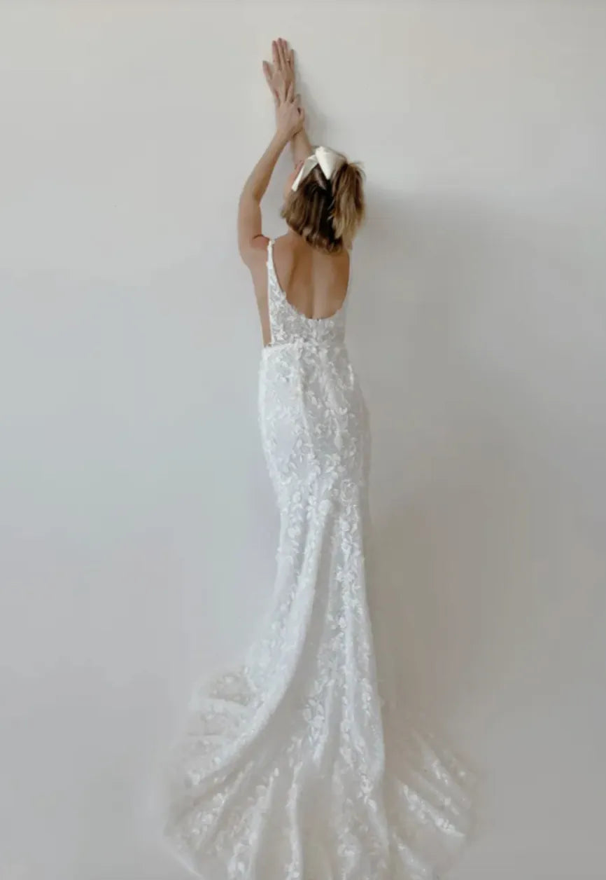 Woman in a white lace wedding dress against a plain background
