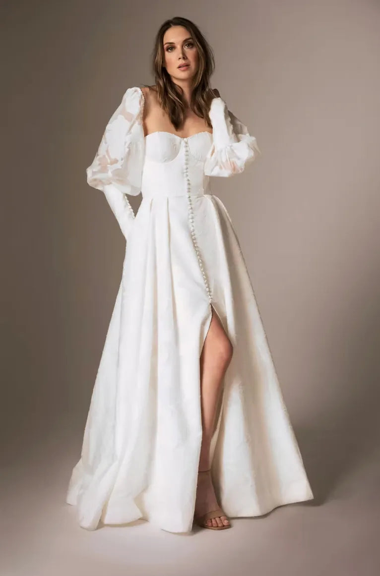 Woman wearing a white wedding dress with long sleeves and a high slit on a brown background