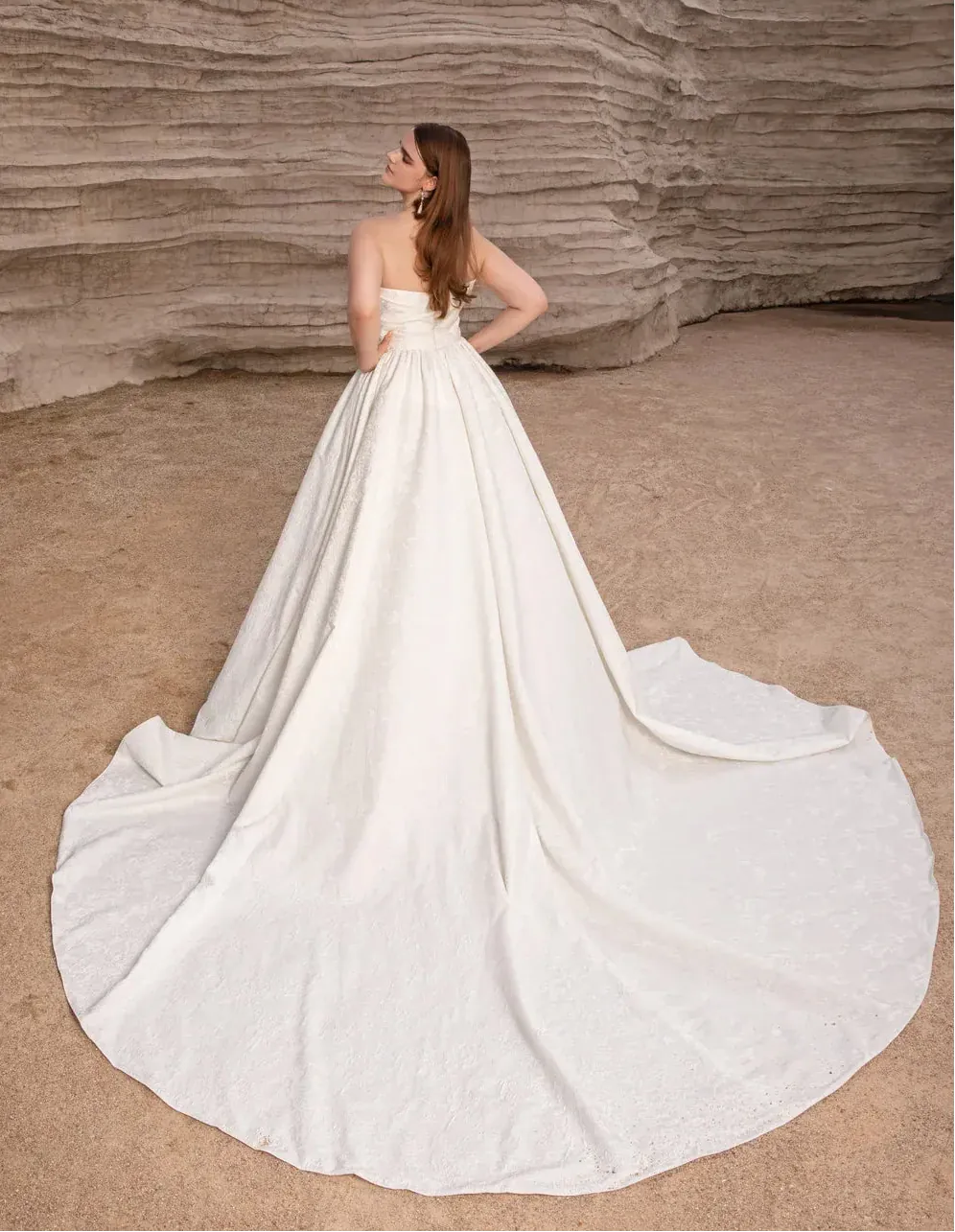 Woman in a white wedding dress standing in a desert landscape with rock formations.