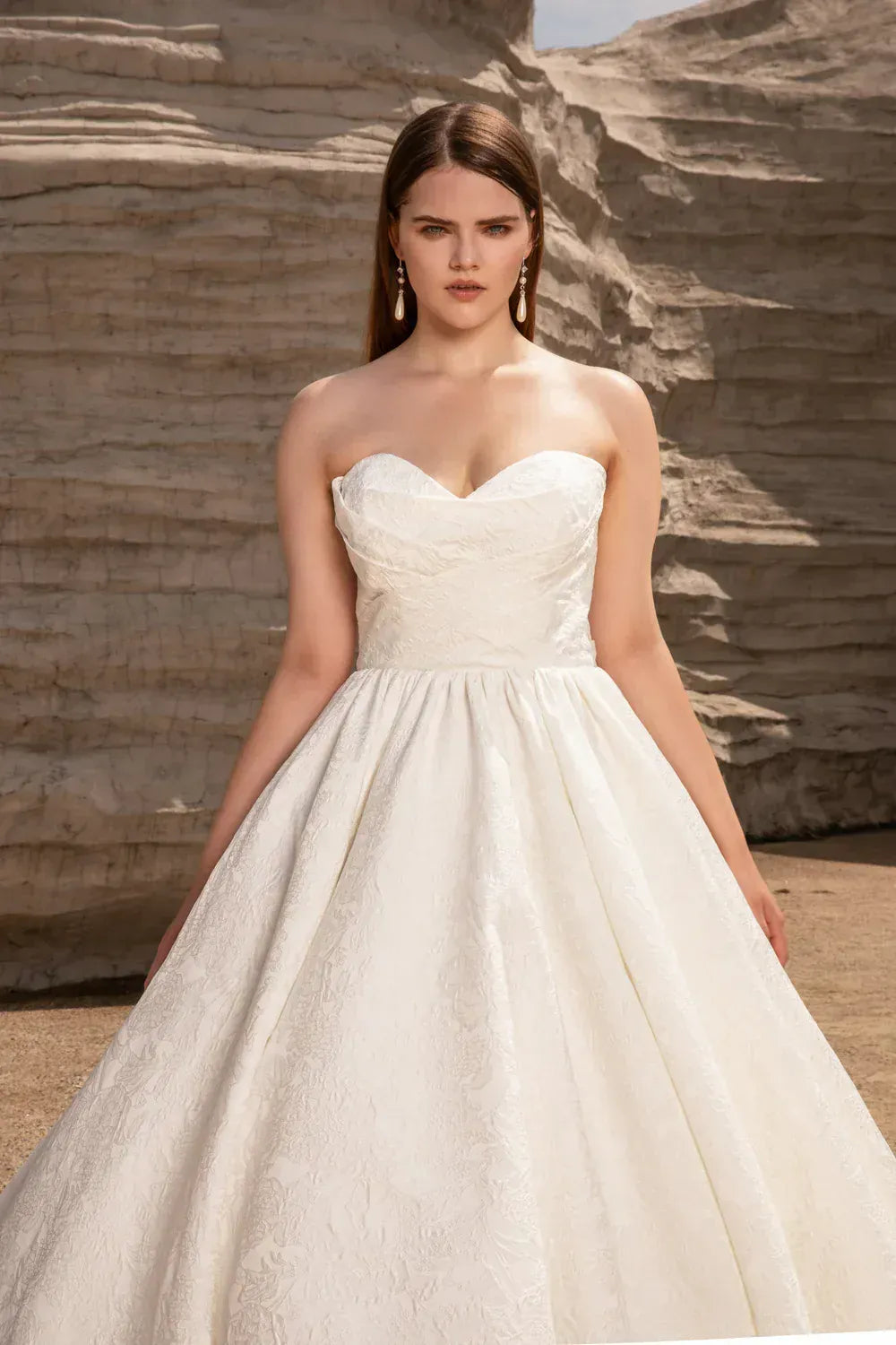 Woman wearing a strapless wedding dress against a stone wall background