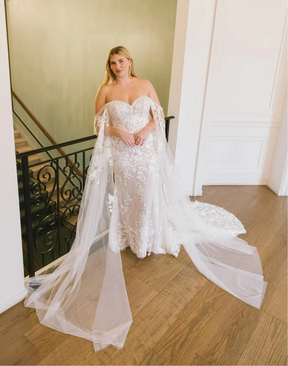 Woman in a white lace wedding dress with a long train standing in a staircase.