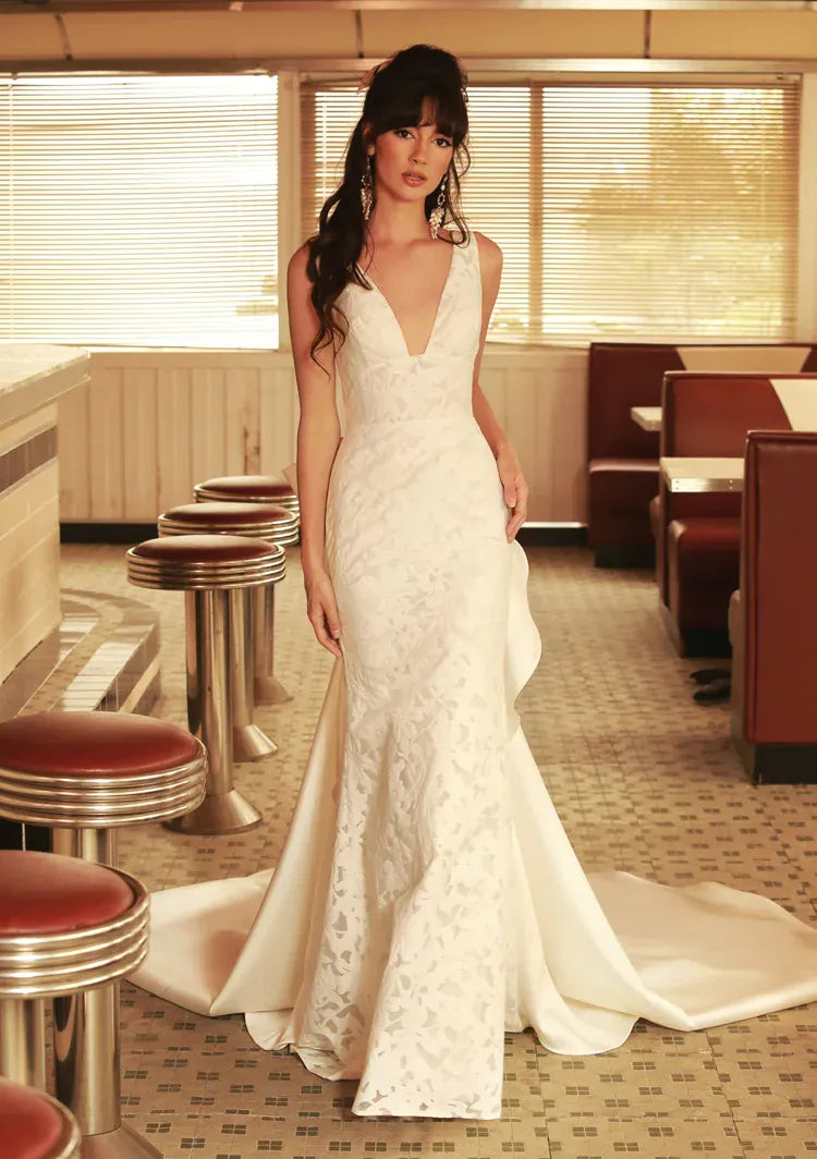 A woman modeling a white lace mermaid-style wedding gown in a retro diner interior with booths, stools, and warm window light.