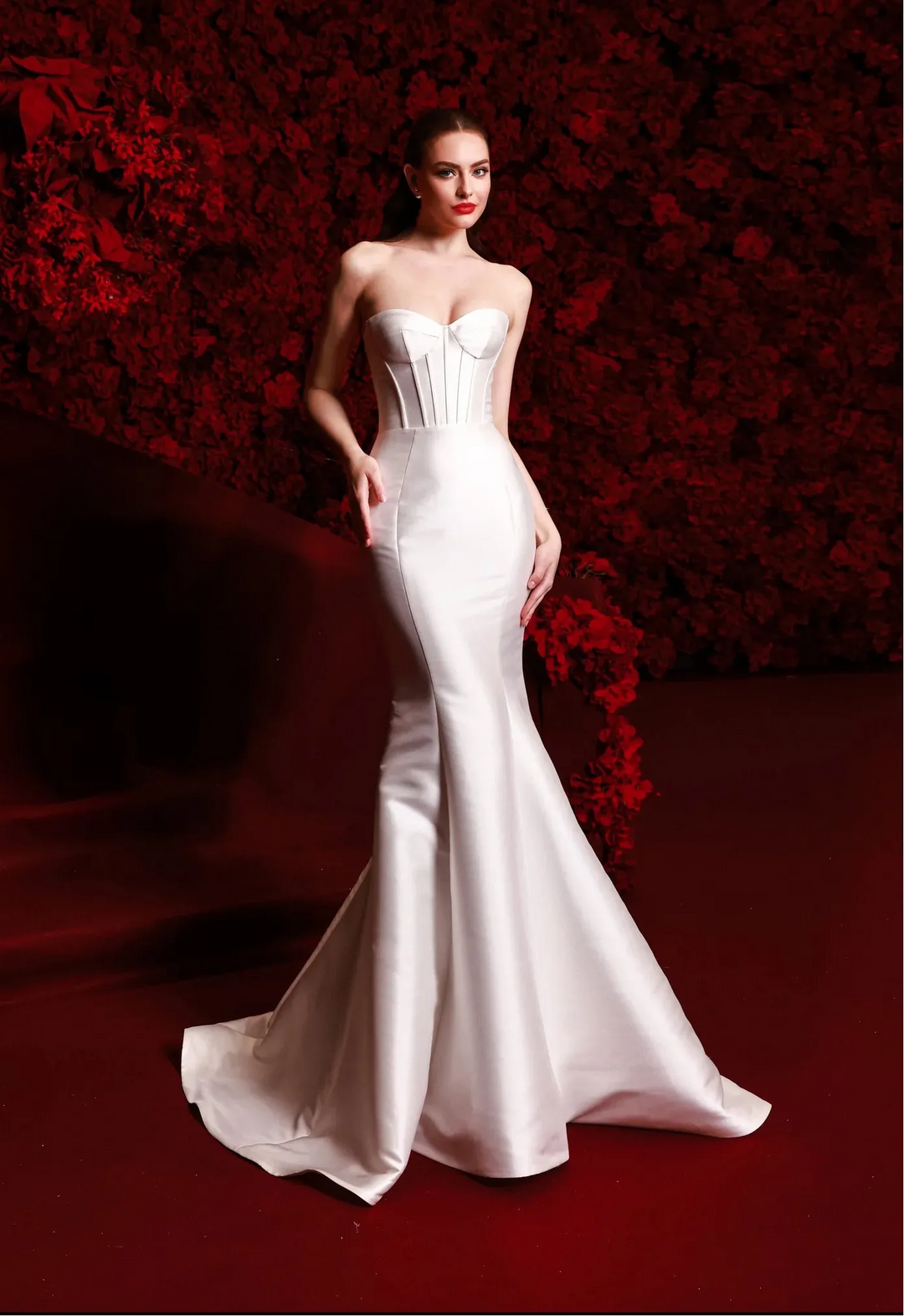 Woman in a white strapless gown against a red floral background