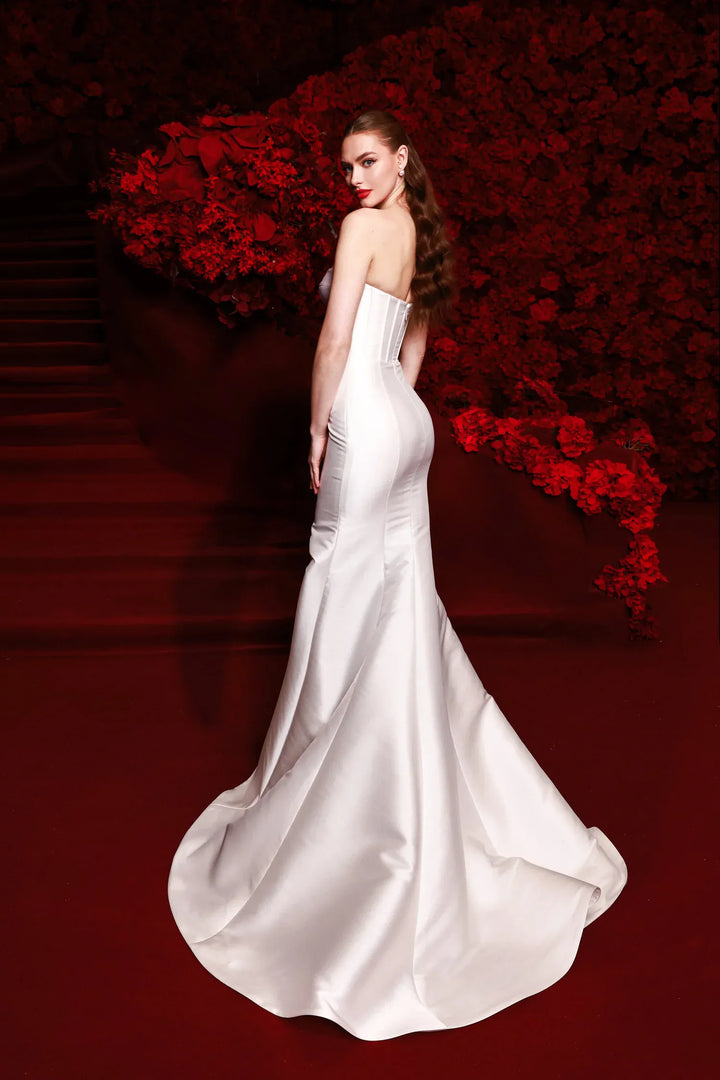 Woman in a white strapless gown standing against a red floral background
