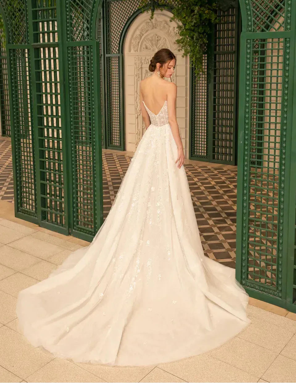 Woman in a white wedding dress standing in front of a decorative green archway.