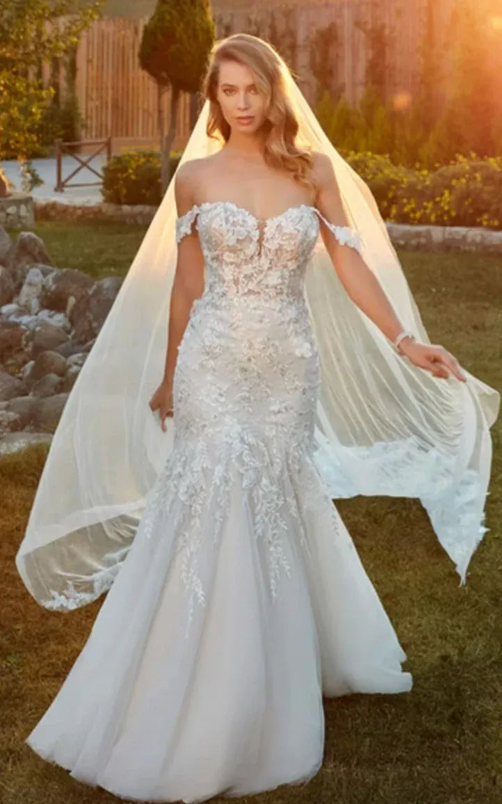 Woman in a white wedding dress with a veil standing outdoors.