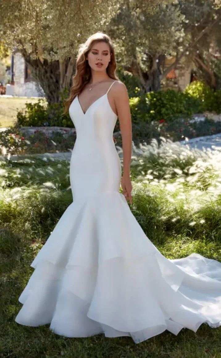 Woman in a white wedding dress standing outdoors with trees and grass in the background