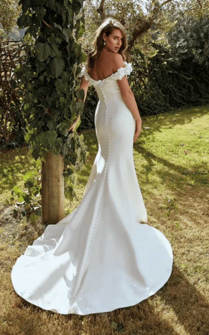 full back of eddy k tilly ivory mikado fit and flare wedding dress with an off the shoulder neckline accents with florals, and a chapel length train