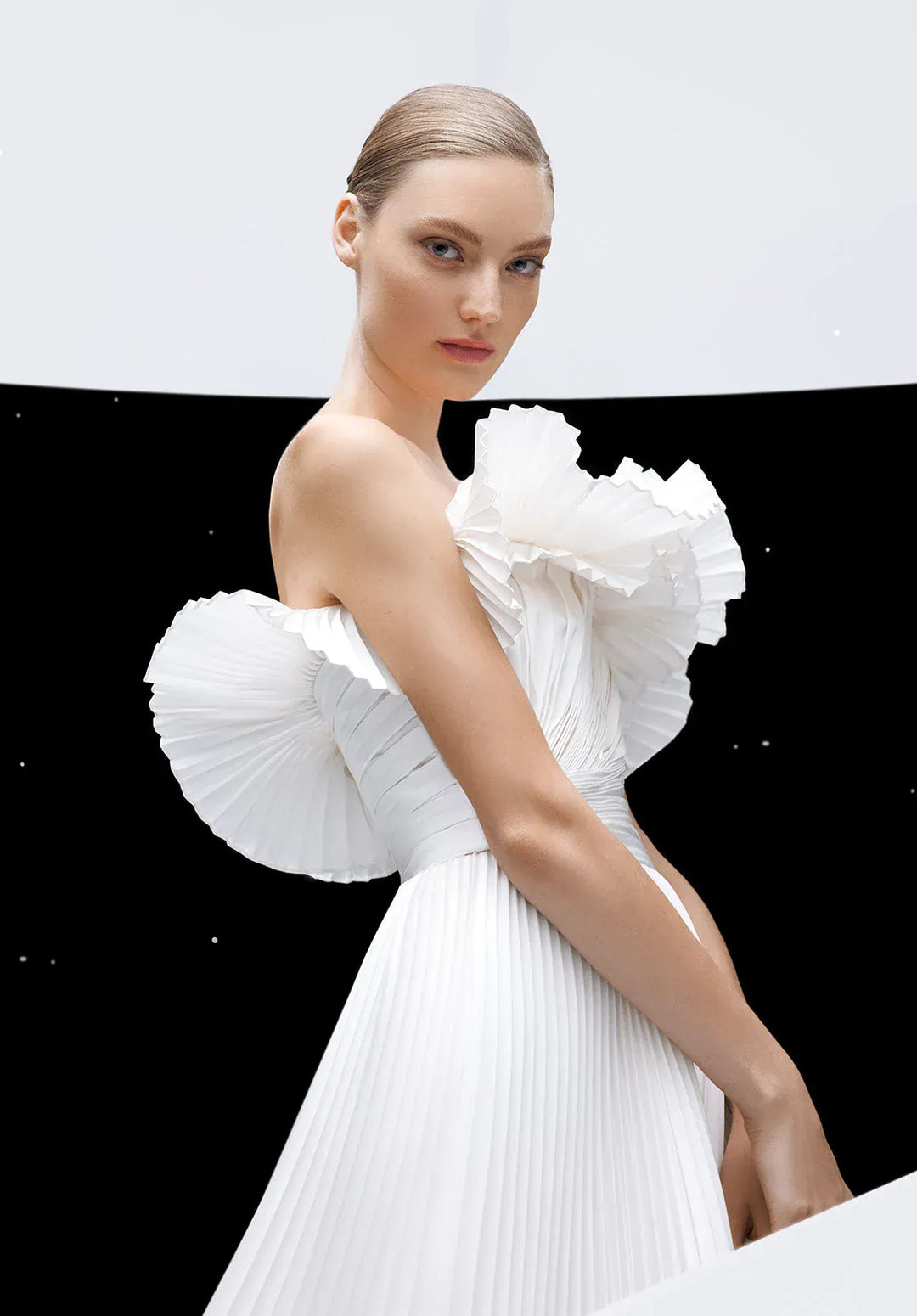 Model wearing a white dress with ruffled shoulders against a black and white background