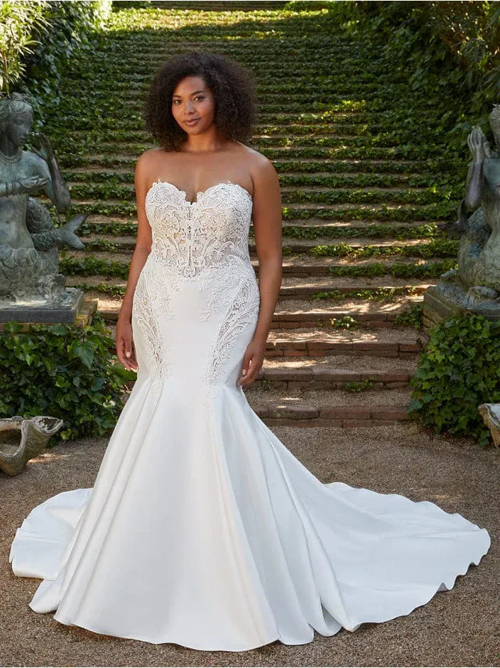 Woman in a white lace wedding dress standing outdoors with greenery and steps in the background