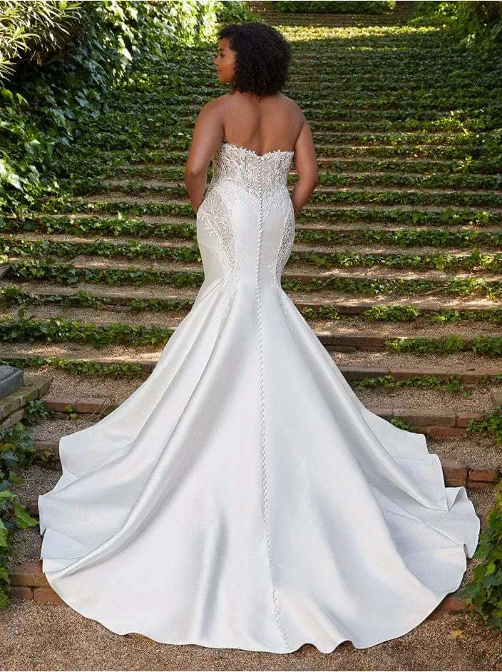 Woman in a white wedding dress standing on stone steps with greenery.
