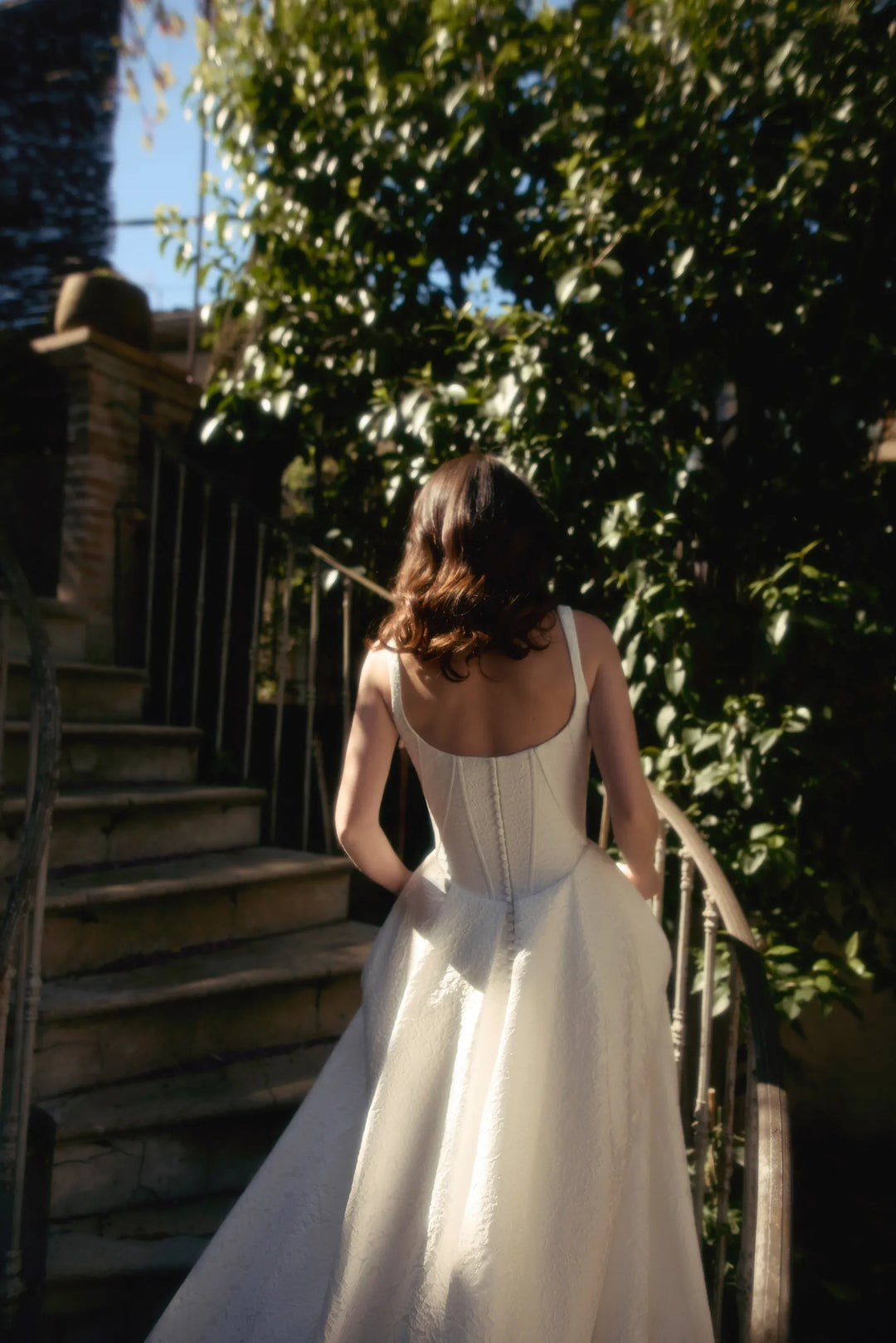 Woman in a white dress walking up a set of stairs with greenery in the background
