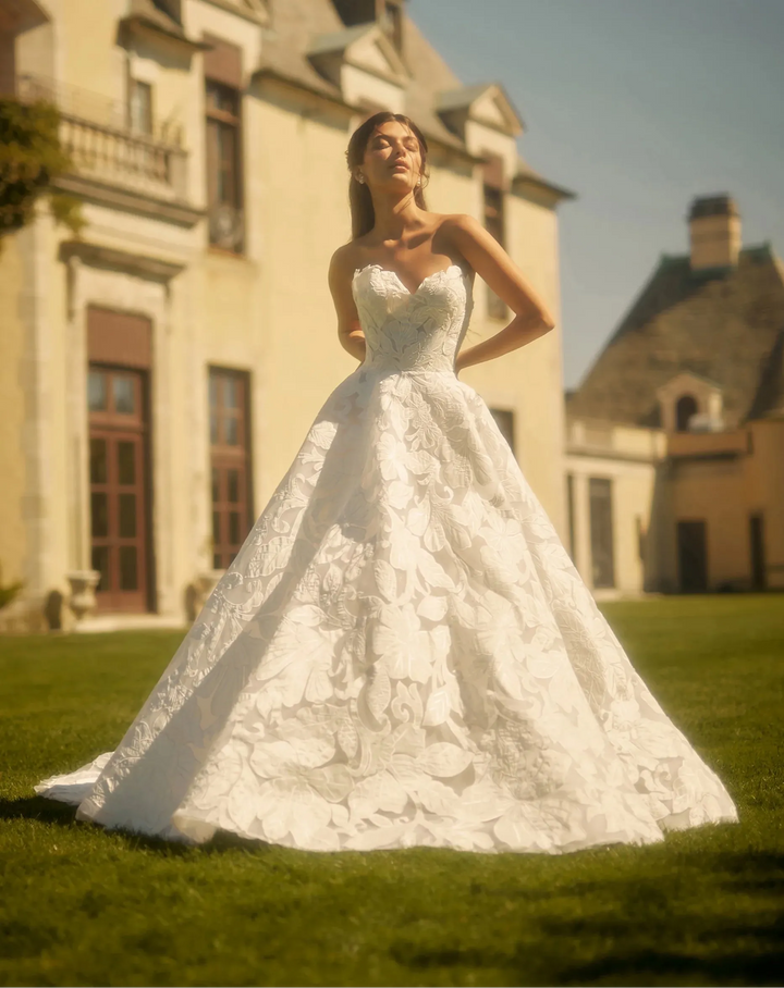 Woman in a white wedding dress standing in front of a large building with a green lawn.