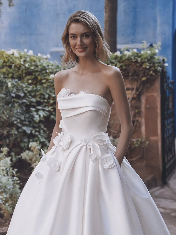 Woman wearing a white strapless gown with floral details in an outdoor setting.