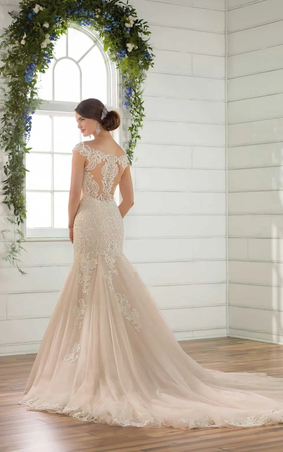 Woman in a lace wedding dress standing in front of a floral archway.