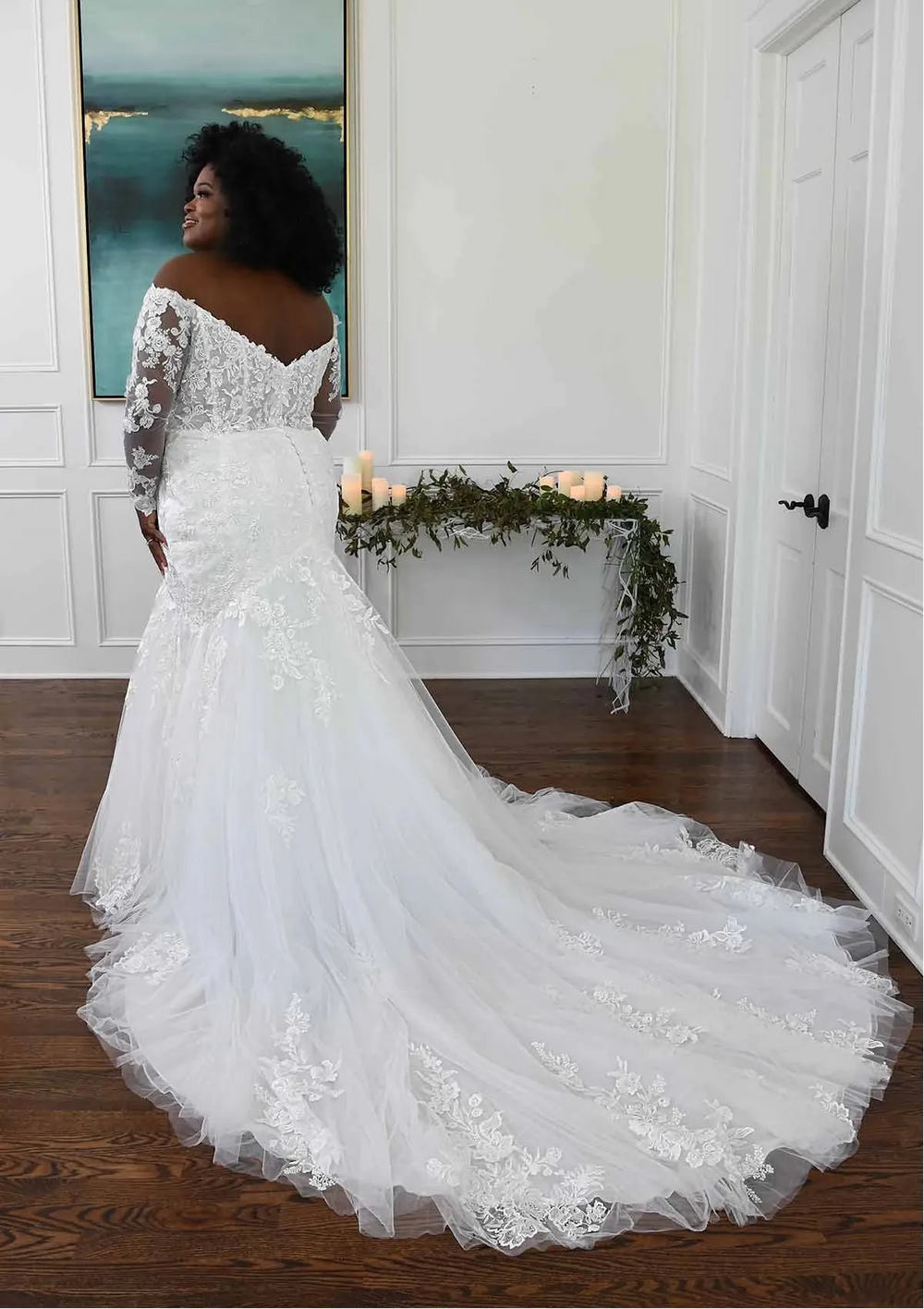 Woman in a white wedding dress standing in a room with a painting on the wall.