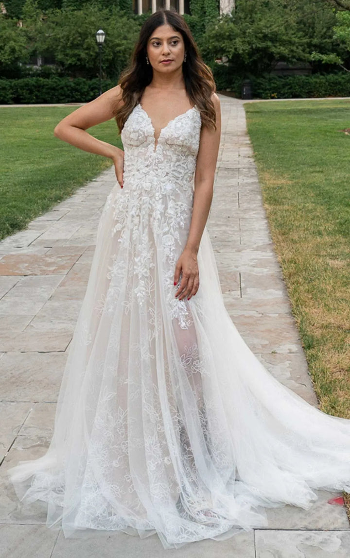 Woman in a white lace wedding dress standing on a pathway outdoors.